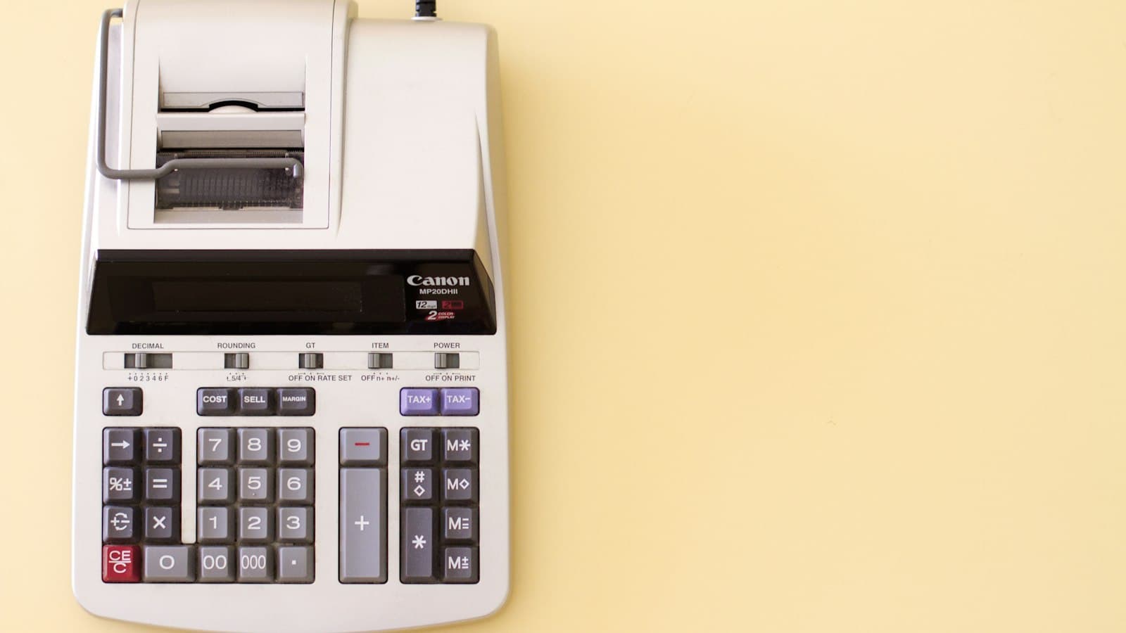 A grey printing calculator on a pale yellow desk