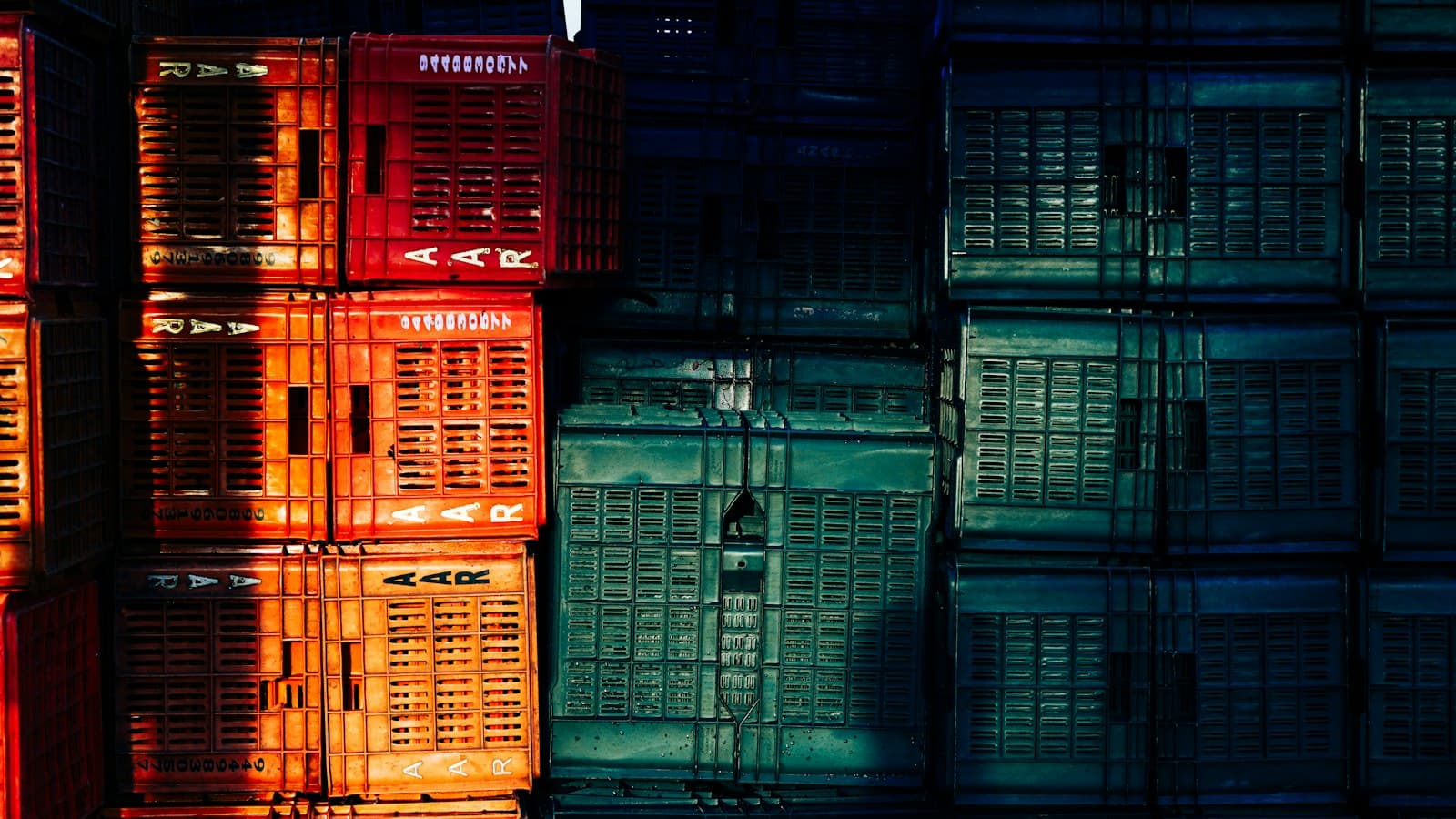 Red and green plastic crates stacked high, half in sunlight and half in shadow