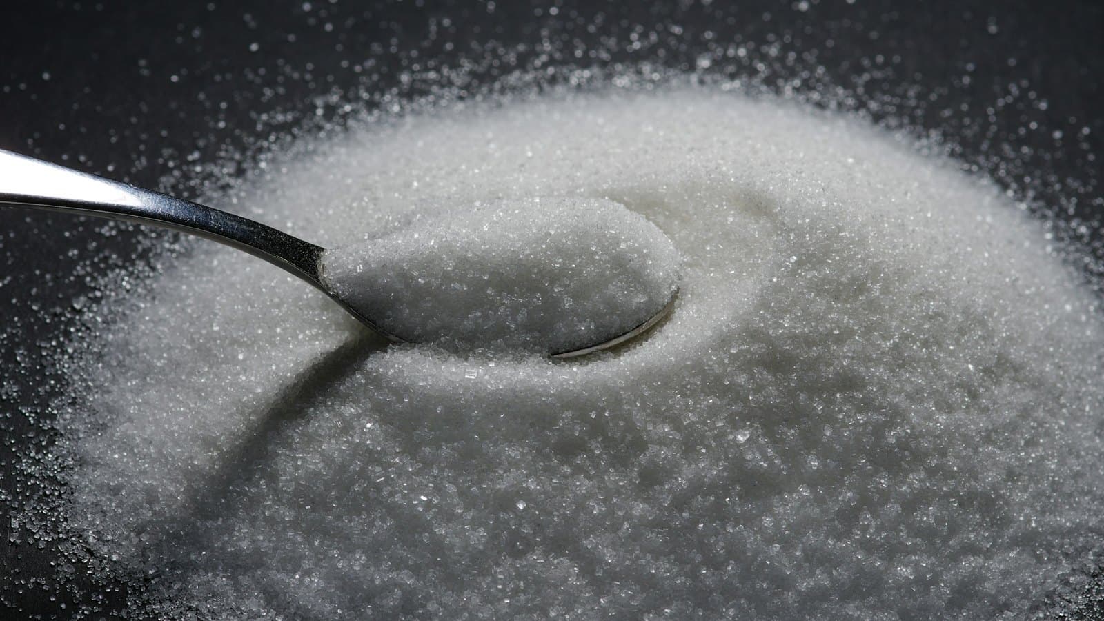 A spoon resting in a heap of white granulated sugar